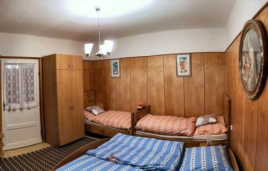 Ložnice obložená dřevem s manželskou postelí a dvěma lůžky v modrém kostkovaném povlečení