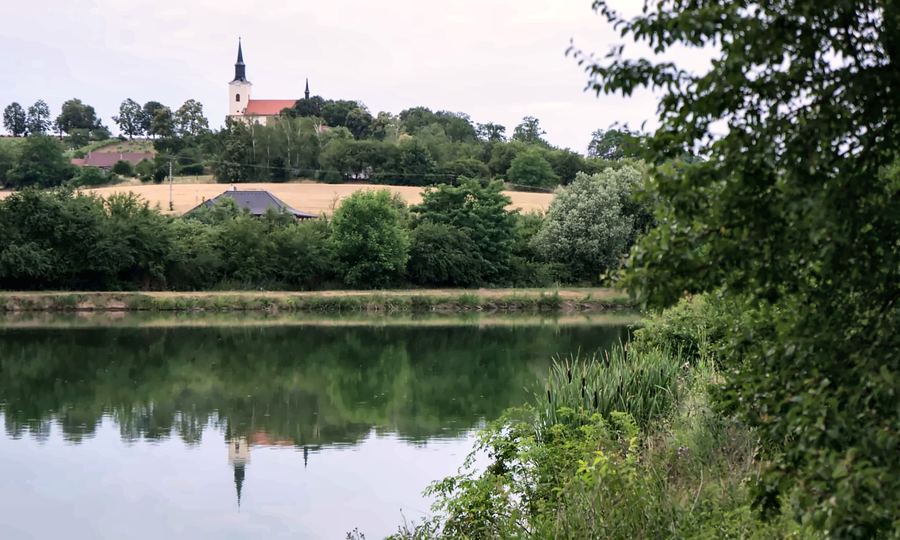 Rybník, nad ním na kopci kostel mezi poli